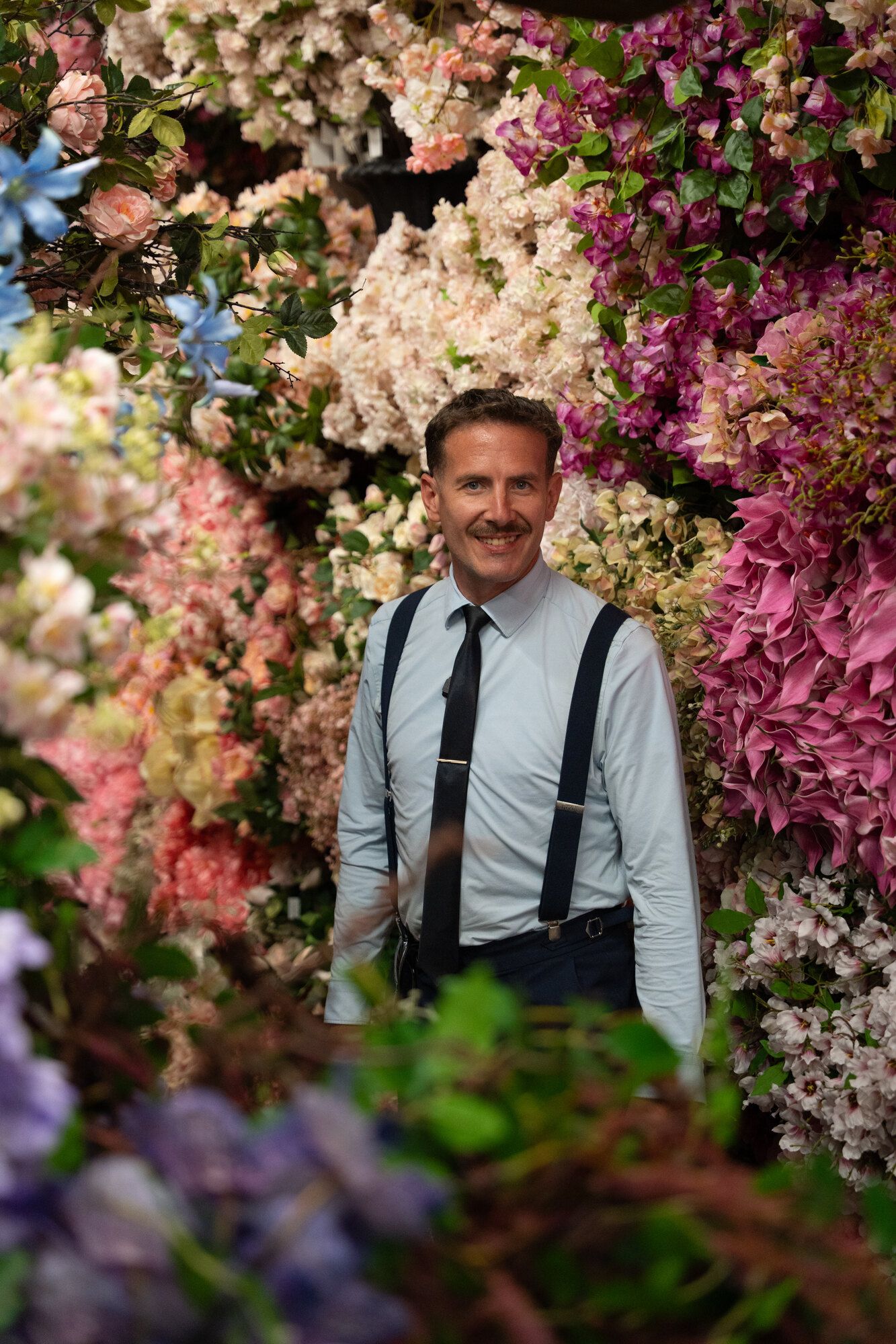 Sébastien Chol devant un mur de fleurs de soie roses et magenta